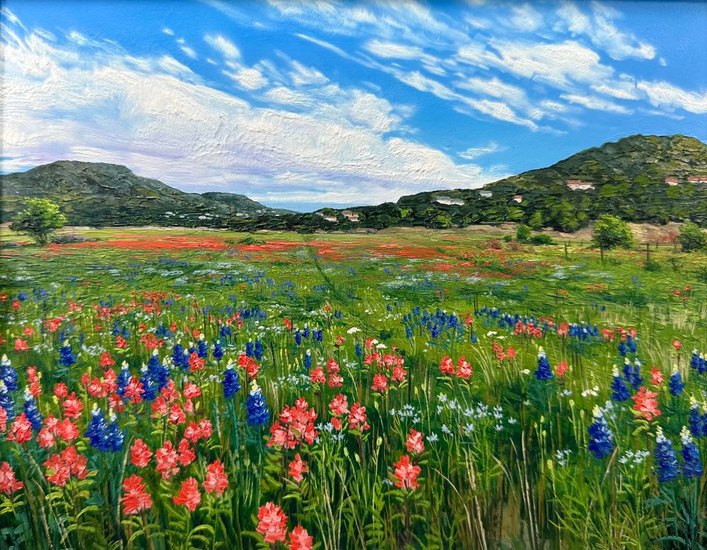 Oil painting of wildflowers in an immense field that slants back to distant hills and the blue cloud streaked sky beyond. 