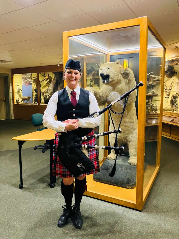 Person in a pink kilt holding bagpipes and standing next to a taxidermied polar bear — jfc, what a thing to type 