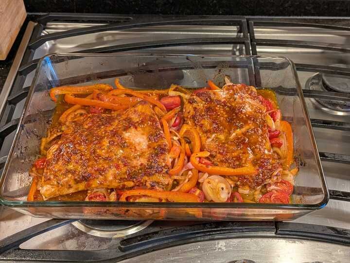 Two pieces of salmon on a shallot and cherry tomato (and red pepper) layer, now baked for 22 minutes, after marinating in a harrissa, lemon juice, olive oil, soy sauce, ... mix. Recipe from https://cooking.nytimes.com/recipes/1026695-baked-salmon-with-harissa-and-cherry-tomatoes