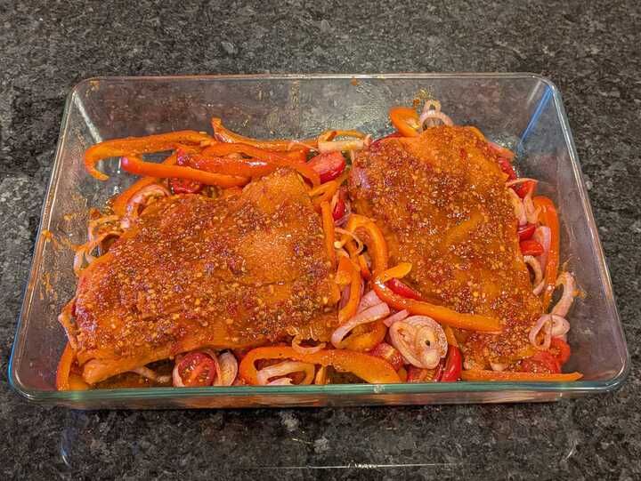 Two pieces of salmon on a shallot and cherry tomato (and red pepper) layer, marinating in a harrissa, lemon juice, olive oil, soy sauce, ... mix. Recipe from https://cooking.nytimes.com/recipes/1026695-baked-salmon-with-harissa-and-cherry-tomatoes