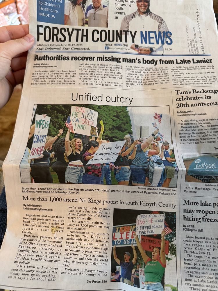 A photograph of the front page of the Forsyth County (GA) News, Midweek edition, June 18/19, 2025. The headline reads "Unified outcry" accompanied by an image of a group of people holding signs in protest which is identified in the caption as a No Kings protest. One prominently featured sign reads "You Can't Be Illegal On Stolen Land."