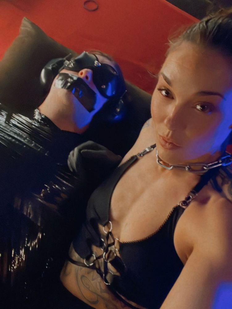 A helpless human lays mummified and fully immersed in sensory deprivation while Dominatrix Daemon takes a selfie. 