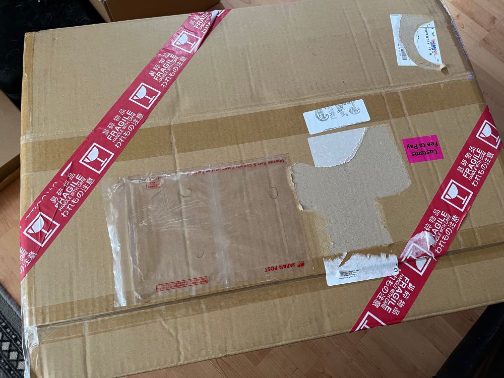 A brown cardboard shipping box with red Japanese fragile tape