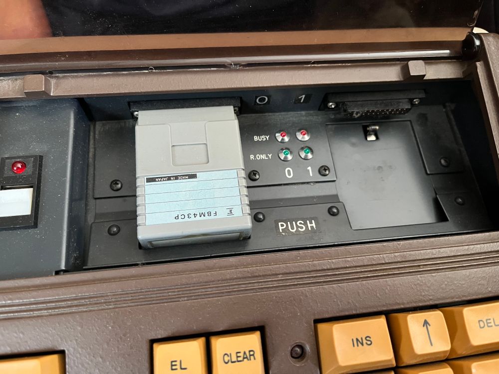 The image shows the interior of an electronic device with a gray cartridge inserted, labeled 