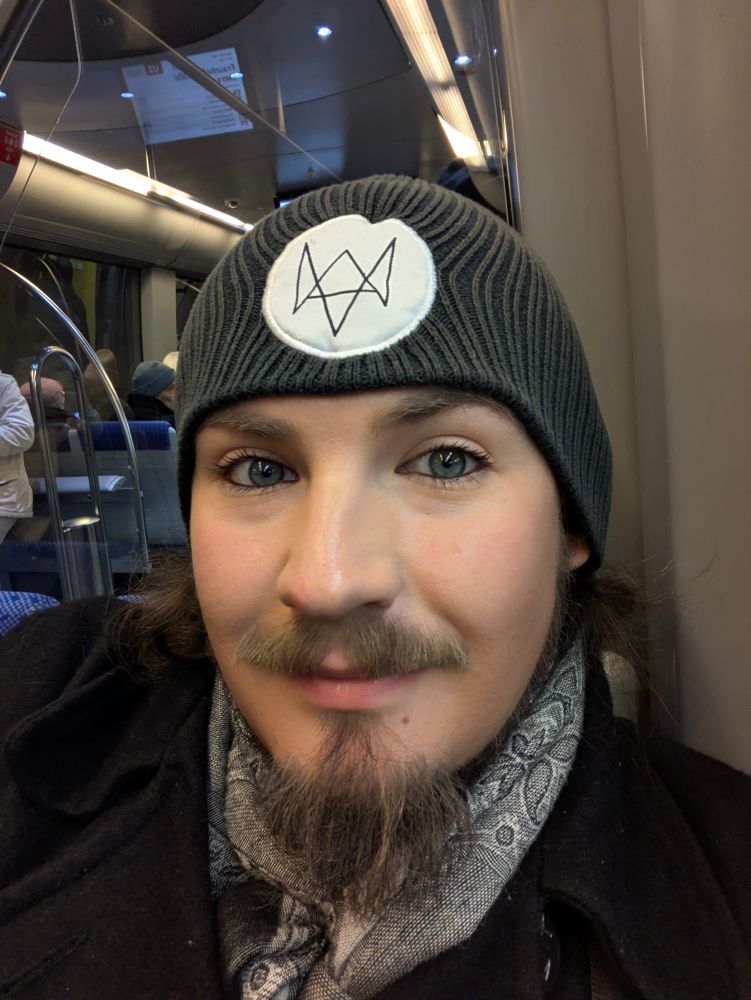 Selfie von mir, einem weißen Mann Anfang dreißig mit Bart und Mütze. Ich bin dezent geschminkt, auffällig sind Kayal und Mascara.