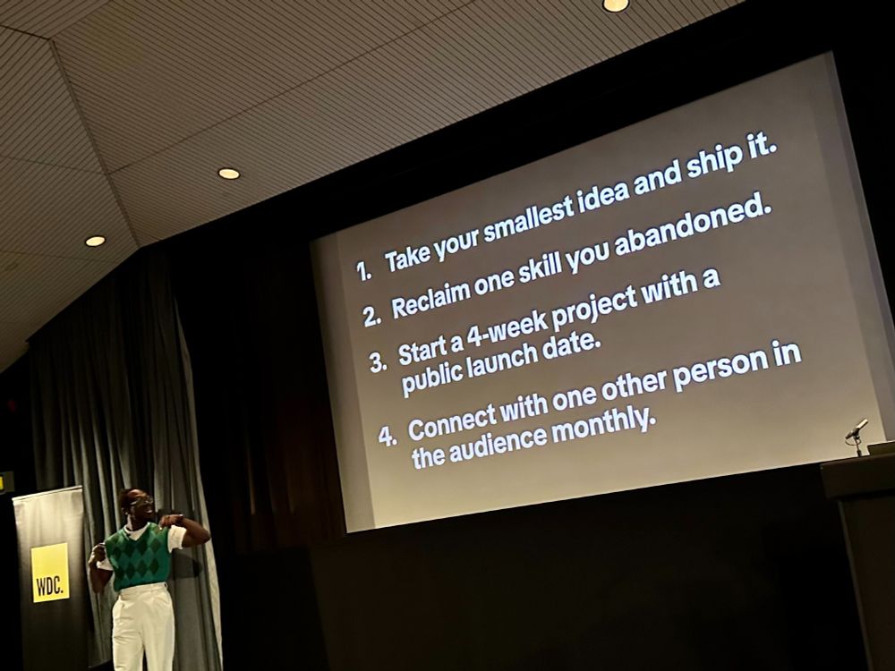 Tey Bannerman speaking at Bristol's Web Dev Conf, impeccably dressed in high-waisted straight leg white trousers, white short sleeved shirt and dark green tank top presenting important life lessons on finding balance between joy and discipline in work to reignite your passion for creativity. 