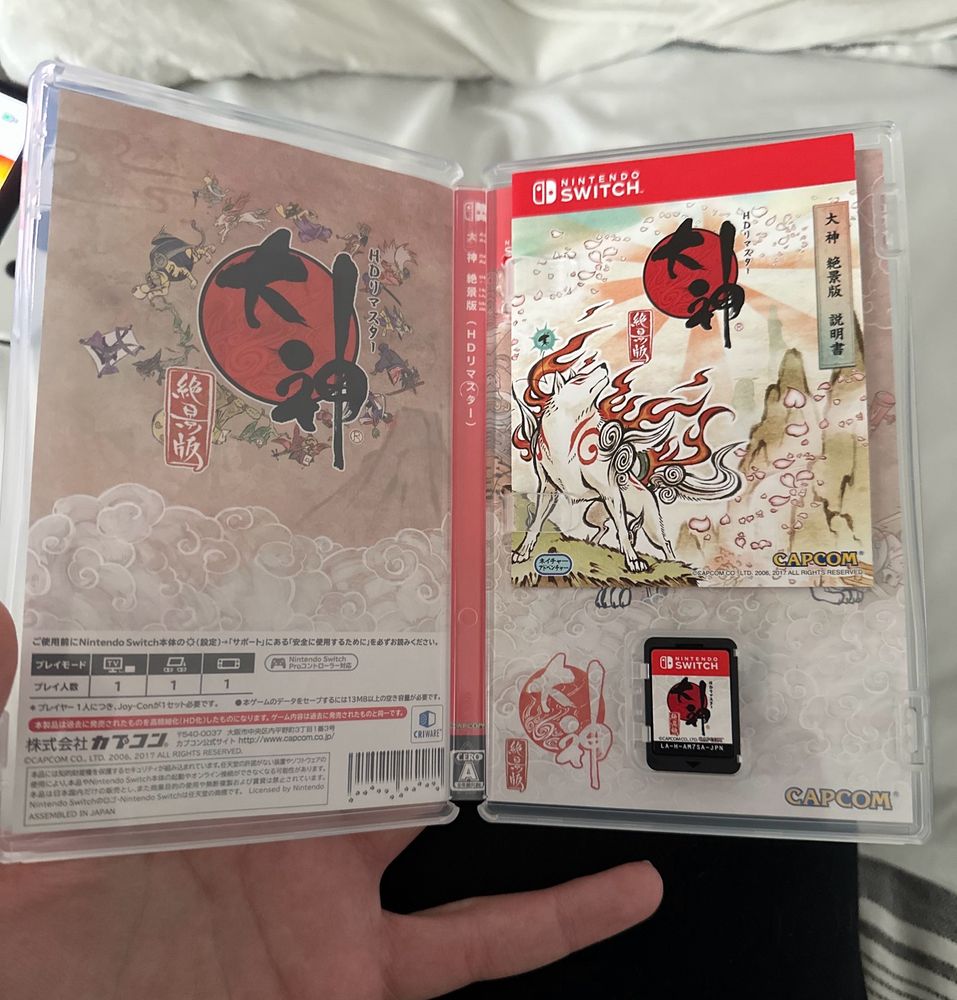 The inside of the game's case is shown with reversible artwork visible, a small manual included, and the game card inside. The photo taker's hand is partially visible near the bottom of the image holding the case open.