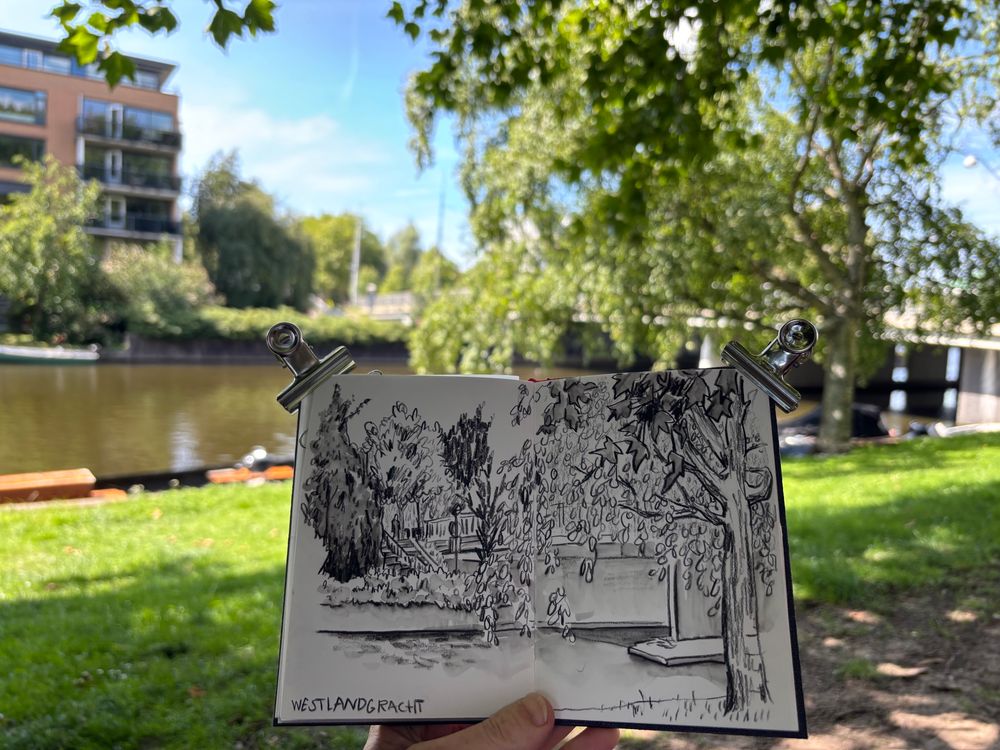 Sketchbook with drawing of canal, with the scene in the background 