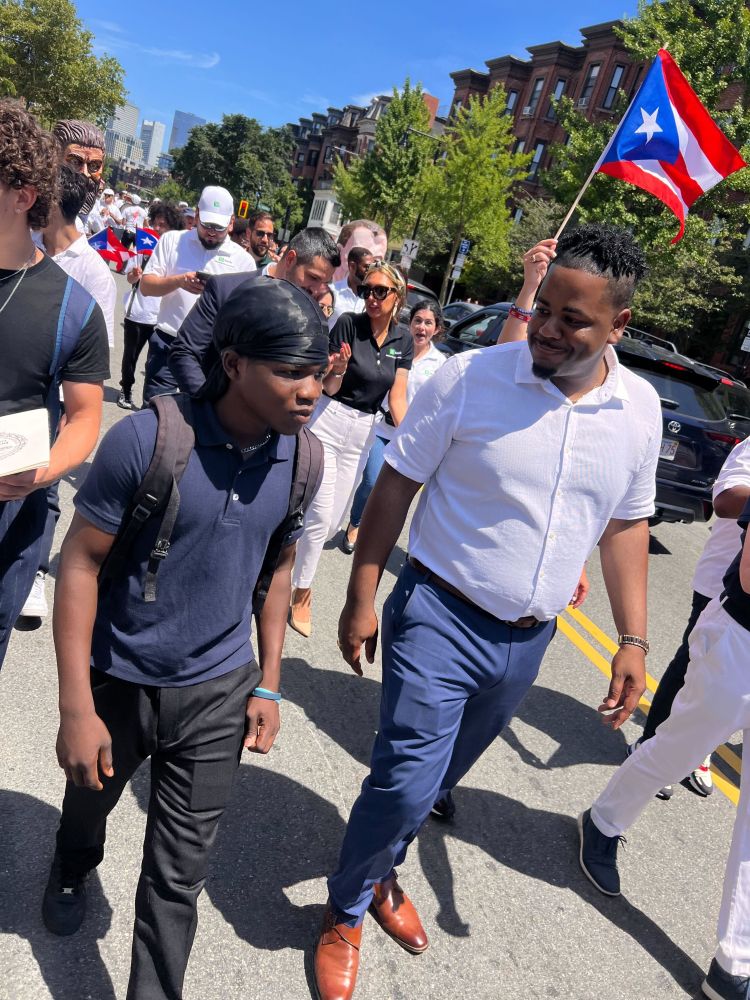 Councilor Santana chatting with a youth during the Festival Betances Parade surrounded by parade marchers