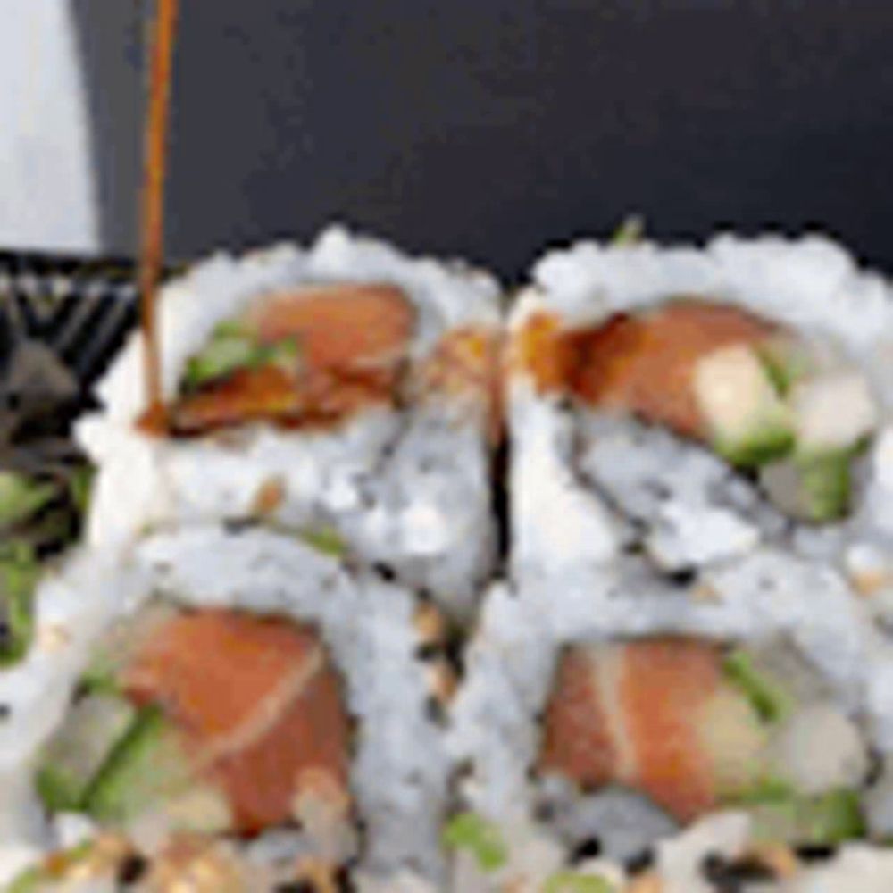 a close up of sushi rolls with sauce being poured over them .