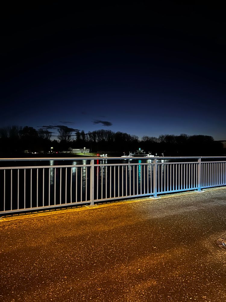 Beleuchteter Zaun. Dahinter der Fluss. 