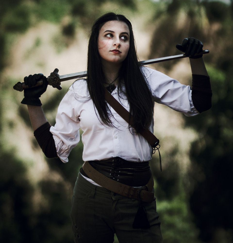 A raven-haired elven woman poses nonchalantly with a sword and a bit of swagger.