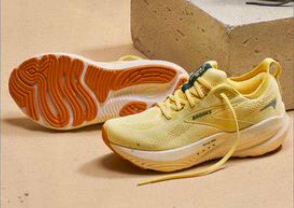A pair of yellowy trainers sit on a yellow surface. You can see the underside of one shoe which looks like bacon.