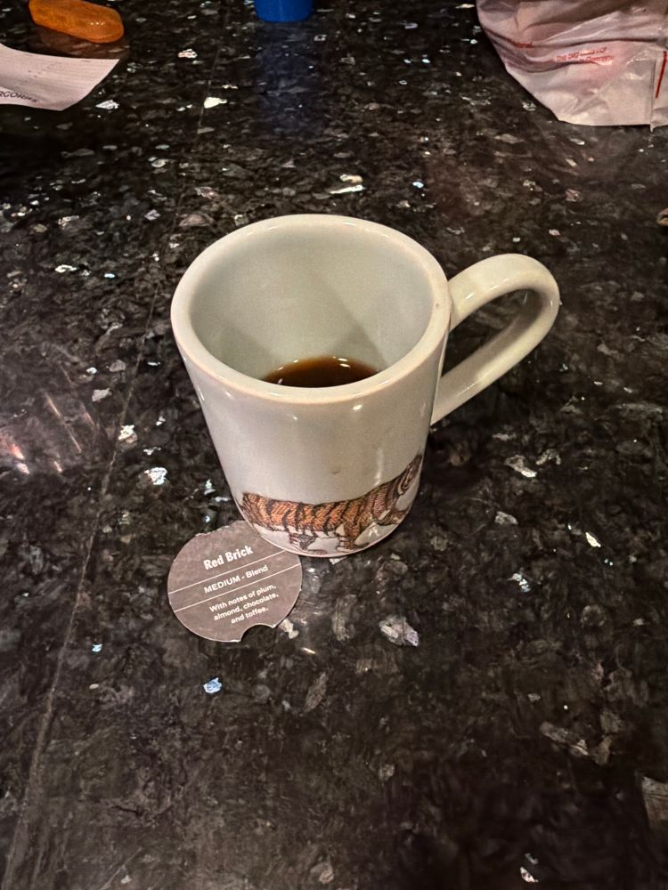 Coffee in a Princeton tiger mug (conference swag, not an alum) along with the tab from a coffee Advent calendar that reads “Red Brick, medium - blend, with notes of plum, almond, chocolate and toffee” 
