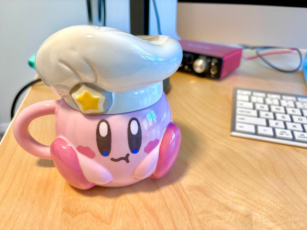 Ceramic Chef Kirby mug that has sculped on feet and arms and a removable ceramic chef hat. It has a painted on face like Kirby is eating someting