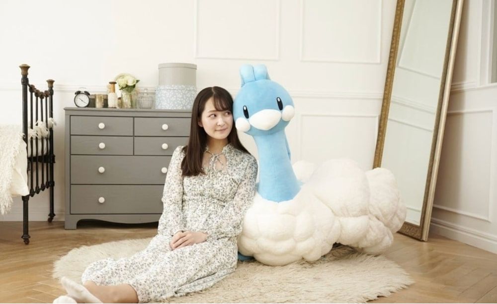 Woman posing in a plainly decorated feminine room with a giant Altaria plush