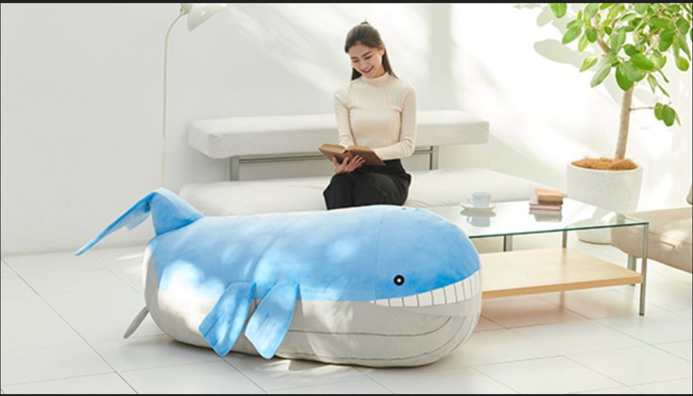 Woman sitting on her minimalist modern sofa reading a book behind a giant Wailord Plush