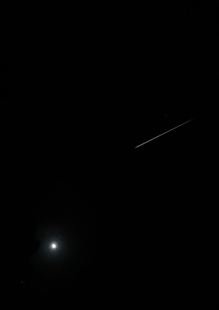 Space capsule streaking over black night sky with near full moon in foreground
