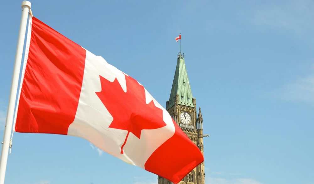 Photo by Jason Hafso on Unsplash. Canadian flag waving in front of the Parliament Building on Parliament Hill in Ottawa.