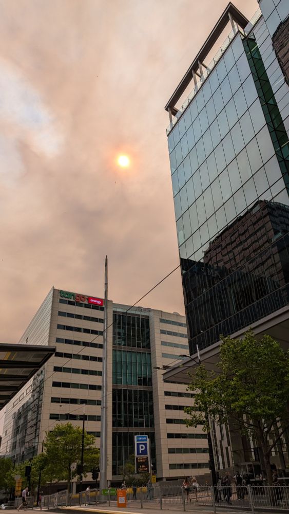 Skyscrapers in the foreground. Above them, the sky is coloured orange-brown with smoke, and the sun is coloured a strange reddish orange. Bushfire smoke over Melbourne.