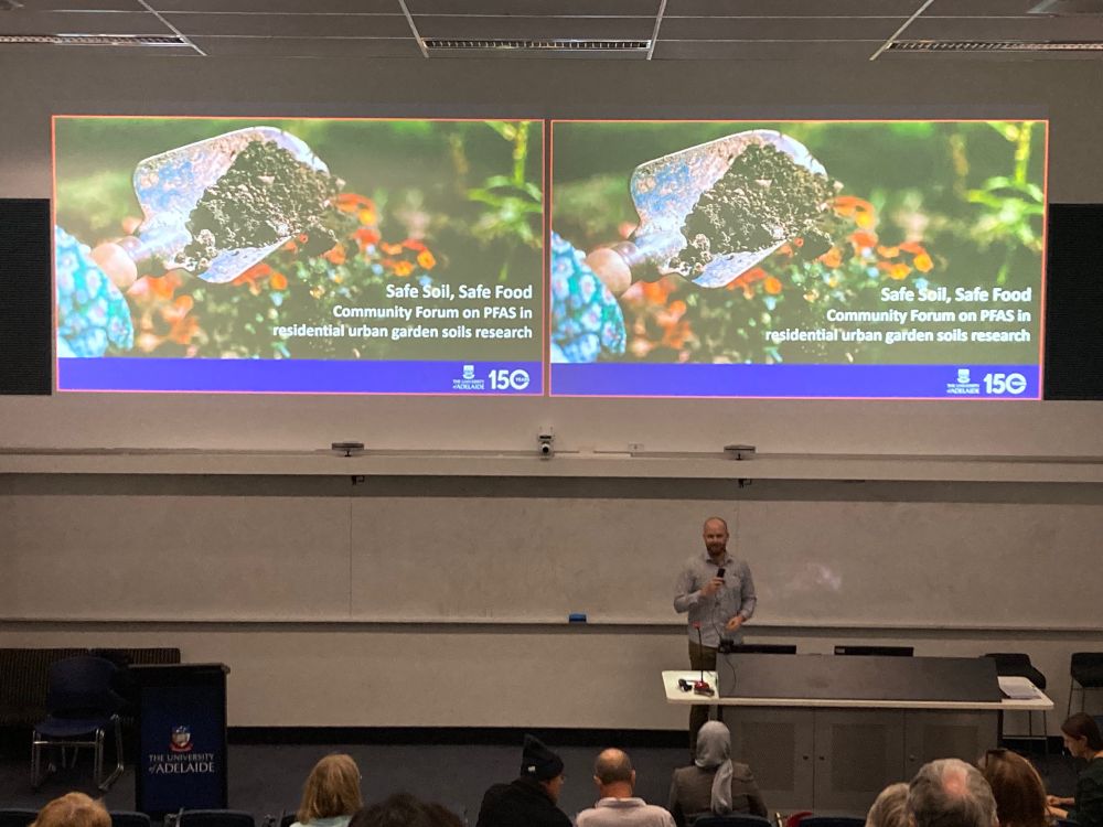 Dr Matthias Salomon at the front of a lecture theatre in front of the title slide “Safe soil, safe food”. 