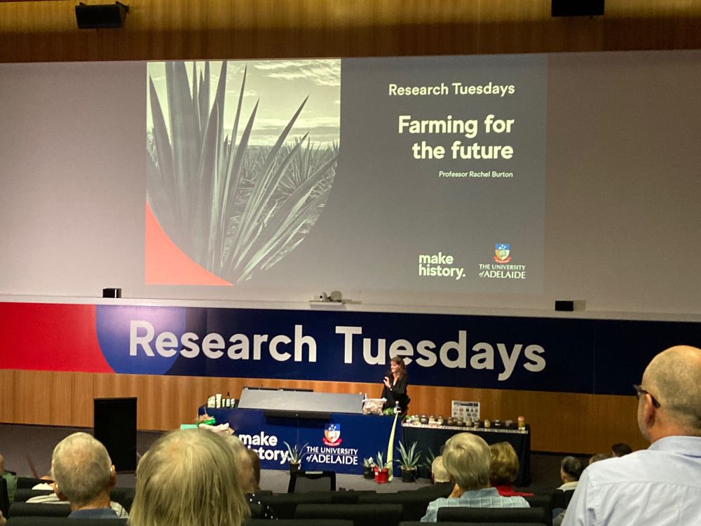 Prof Rachel Burton standing in front of her title PowerPoint slide “Farming for the future” in a lecture theatre. 