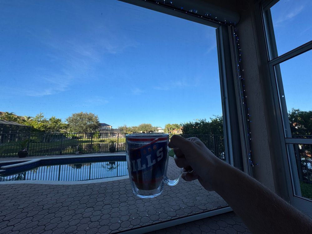 Blue and white LED outline the inside of a covered back pool patio in Florida. A buffalo bills Tervis is held aloft 