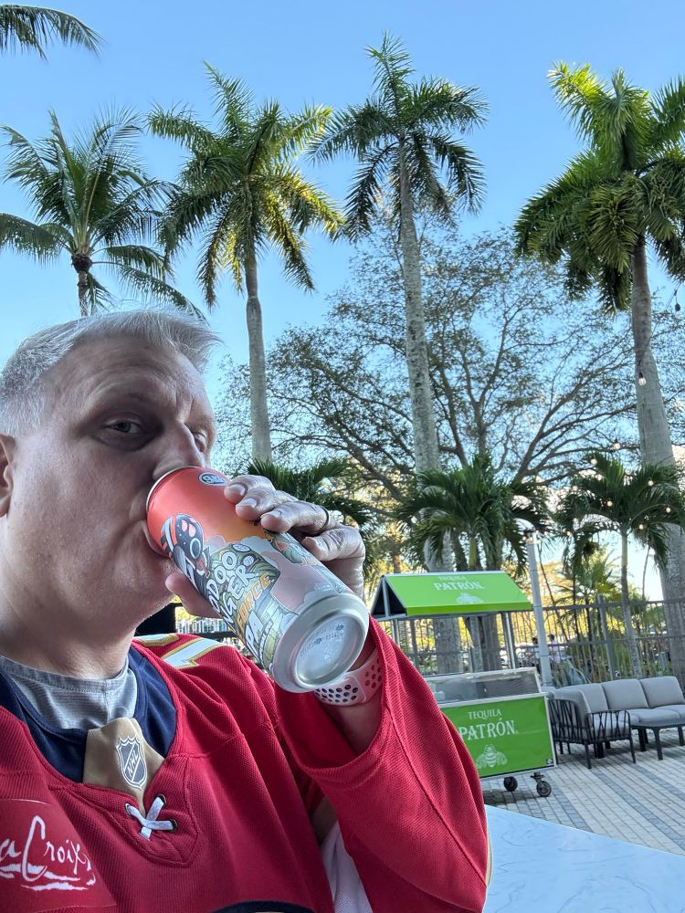 Me drinking a Voodoo Ranger Juice Force IPA outside Amerant Bank Arena with Palm trees. 