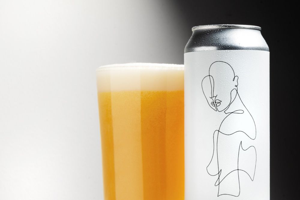A white can with a single black line drawing showing the outline of a human. A glass with bright golden beer is next to it.
