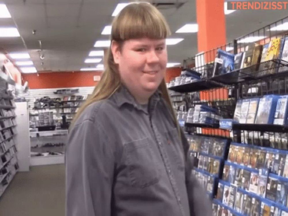 a man with a mullet is standing in front of a shelf of dvds