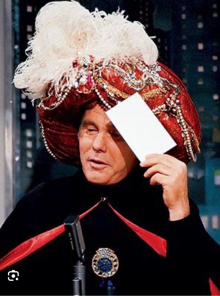 Image of Johnny Carson as “Carnac the Magnificent” holding a sealed envelope to his head. 