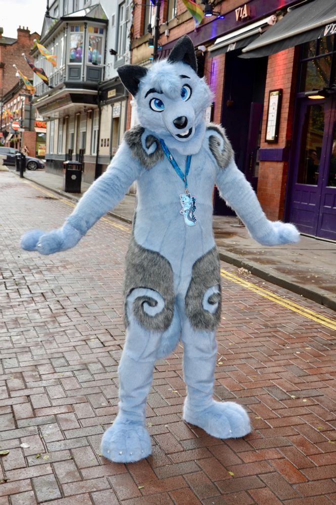 A blue and grey fursuiter posing on a Manchester street.