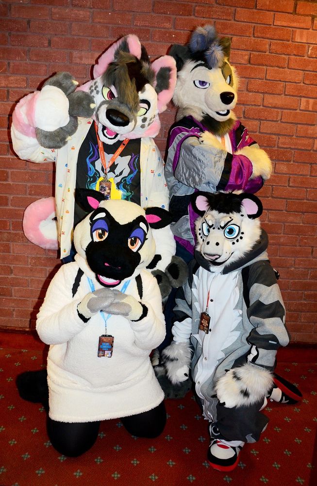 Four fursuiters posing in front of a brick wall.