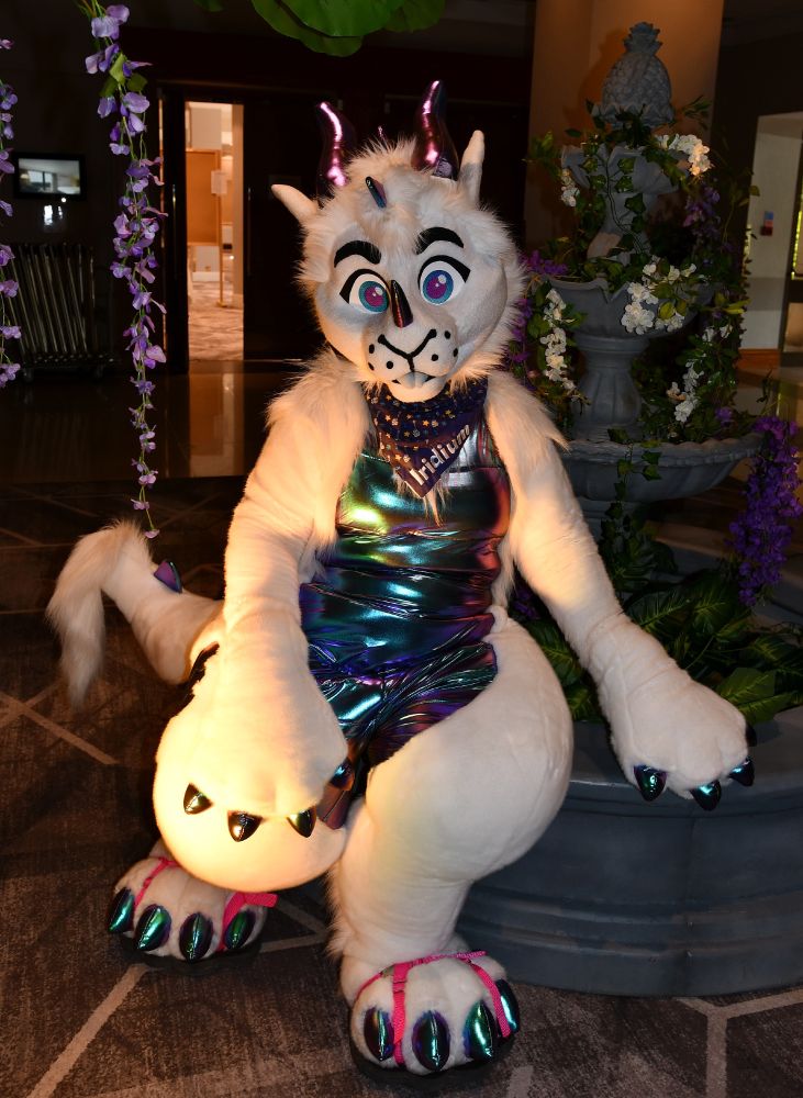 A white dragon with a metallic belly posing by a mock fountain in low light.