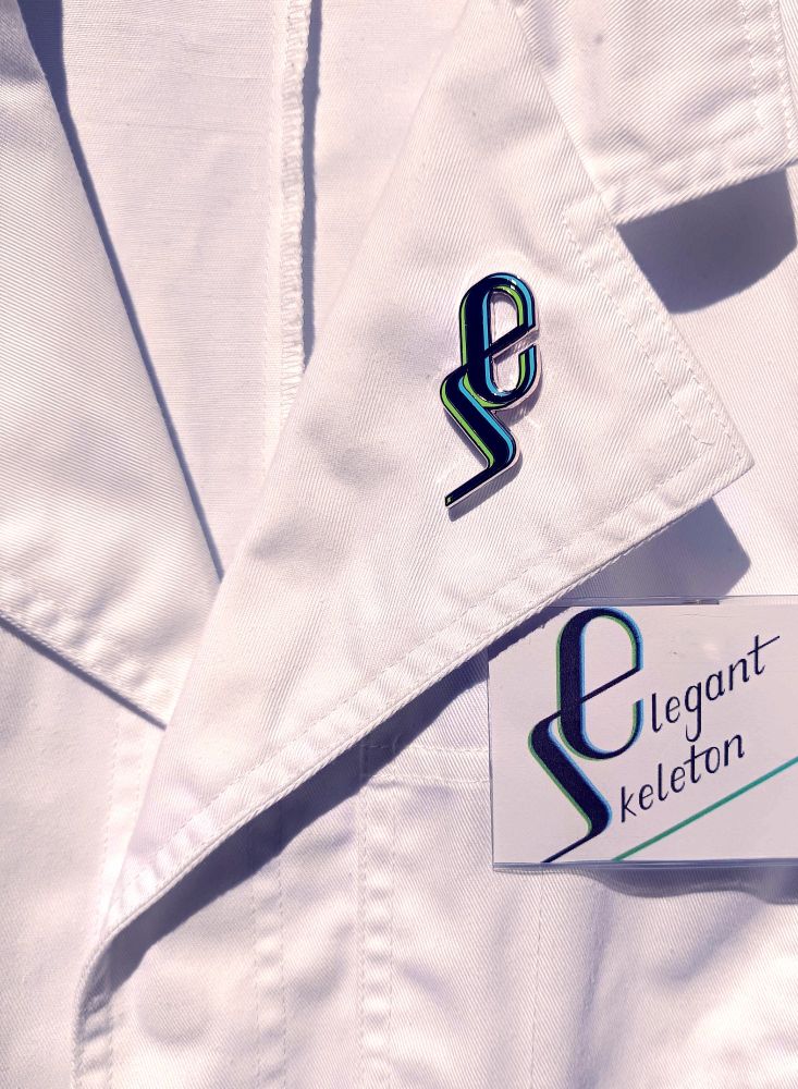 A high quality shiny hard enamel pin of the Elegant Skeleton logo perfectly positioned on a lab coat lapel above a name tag positioned on the pocket of the lab coat