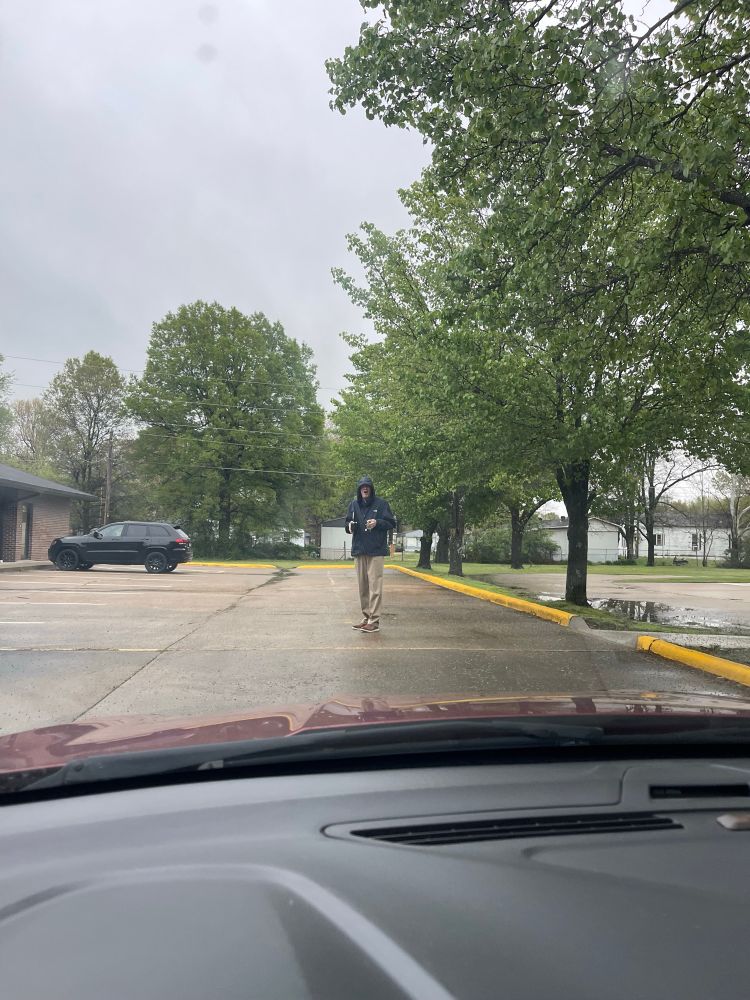 man in a rain jacket with keys and a coffee mug in his hands standing in the middle of the parking lot to block my way in.