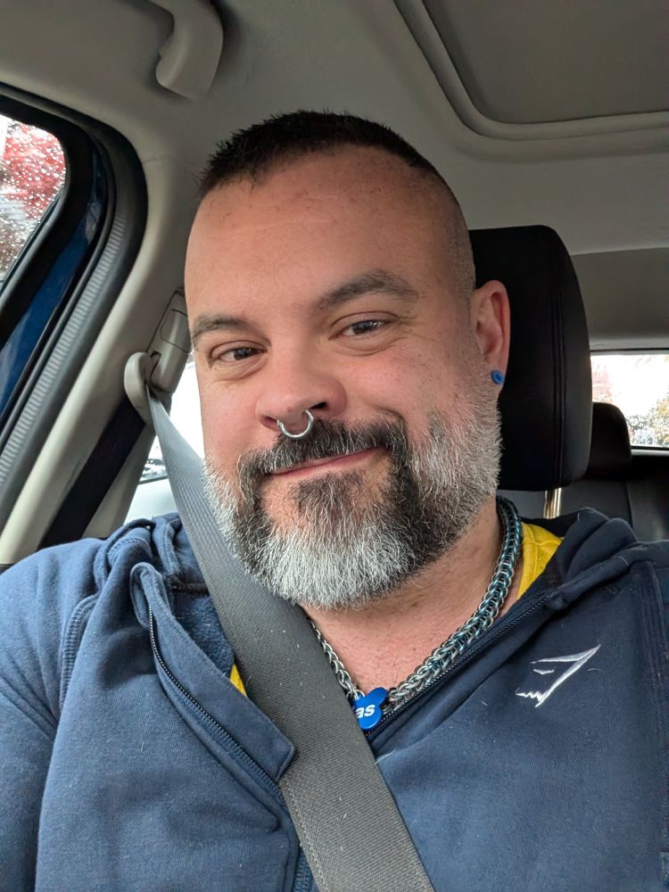 Man in a blue hoodie with a fresh fade.  Septum ring and blue plug earrings