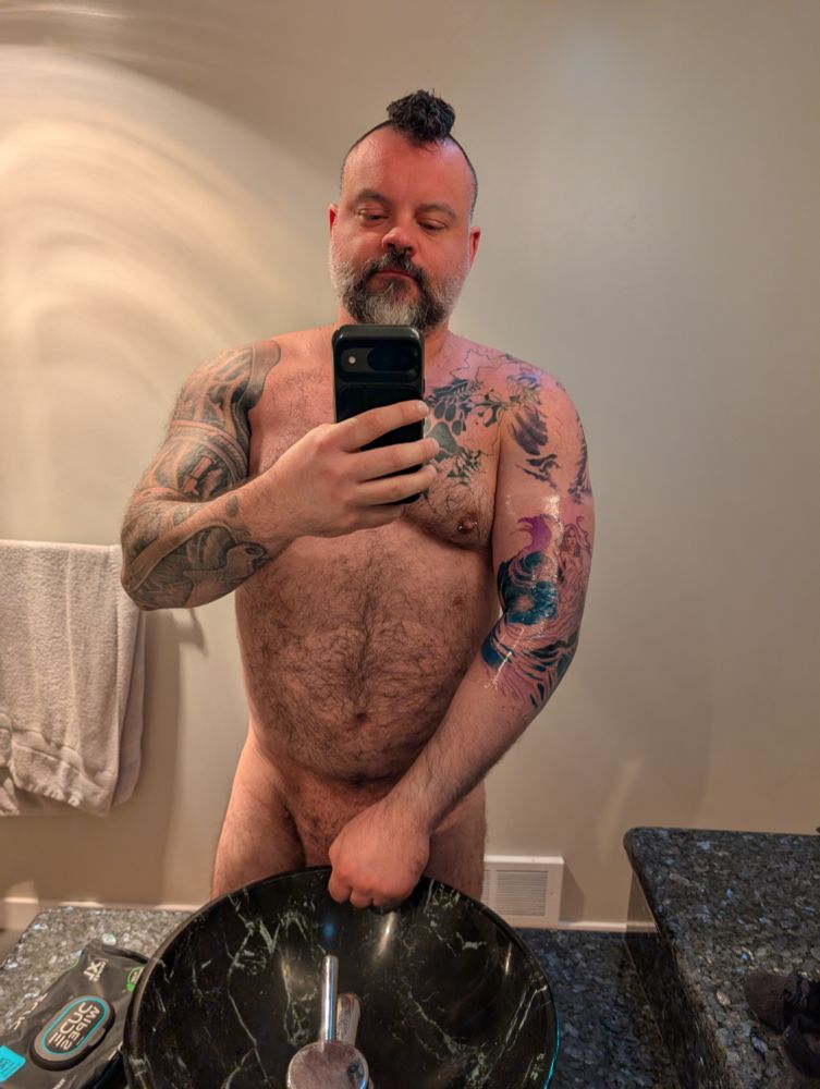 Man standing in the bathroom with a fresh left arm tattoo covered in Tegederm 