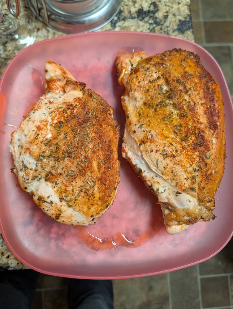 Two freshly cooked turkey breasts with herbs and spices on a red plate