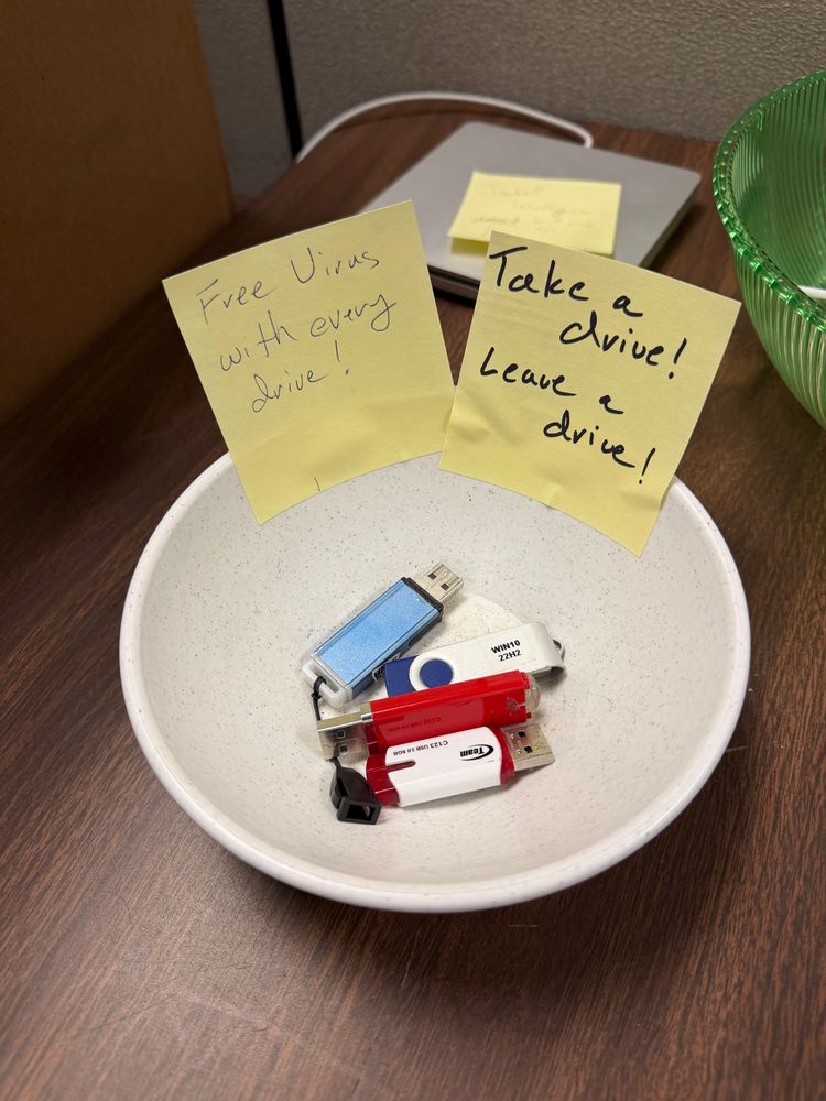 A small bowl containing several flash drives. Two labels are attached to bowl. 