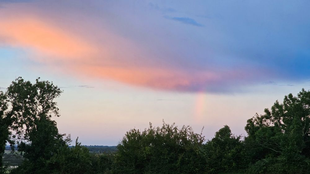 View from a hill, sunset lit cloud with a rainbow coming out of it. 