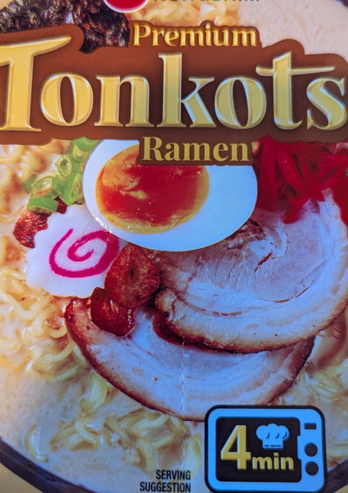 A lid of Tonkotsu ramen, showing a 4 minute microwave time. There is an image of a microwave with a little chef's hat in it to silently mock your 