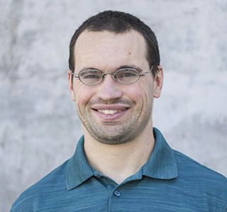 Matt Jennings smiling wearing a blue collared shirt in front of a blurred white and gray background.
