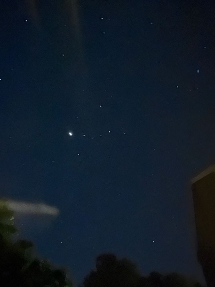 Dark sky with stars, a small smudge of light, and a w-shaped constellation