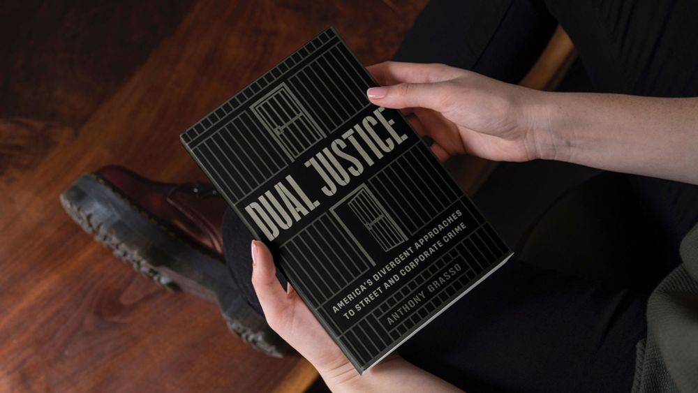 A person's hands holding a book titled "Dual Justice" by professor Anthony Grasso