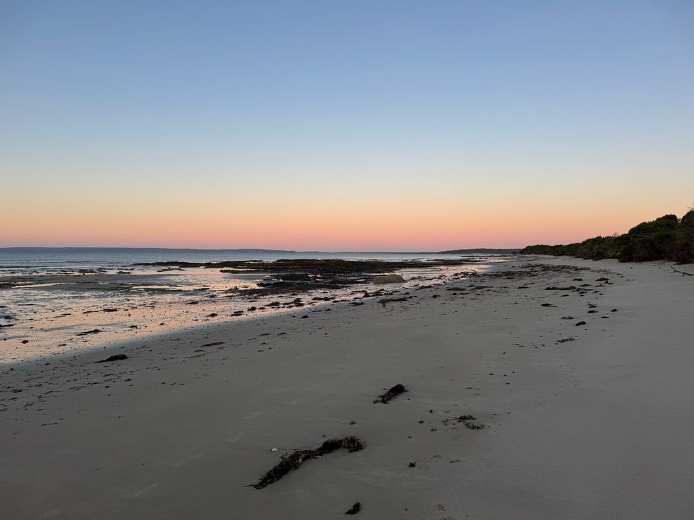 Sandy beach at dusk with purple, pink haze in the skyline. 