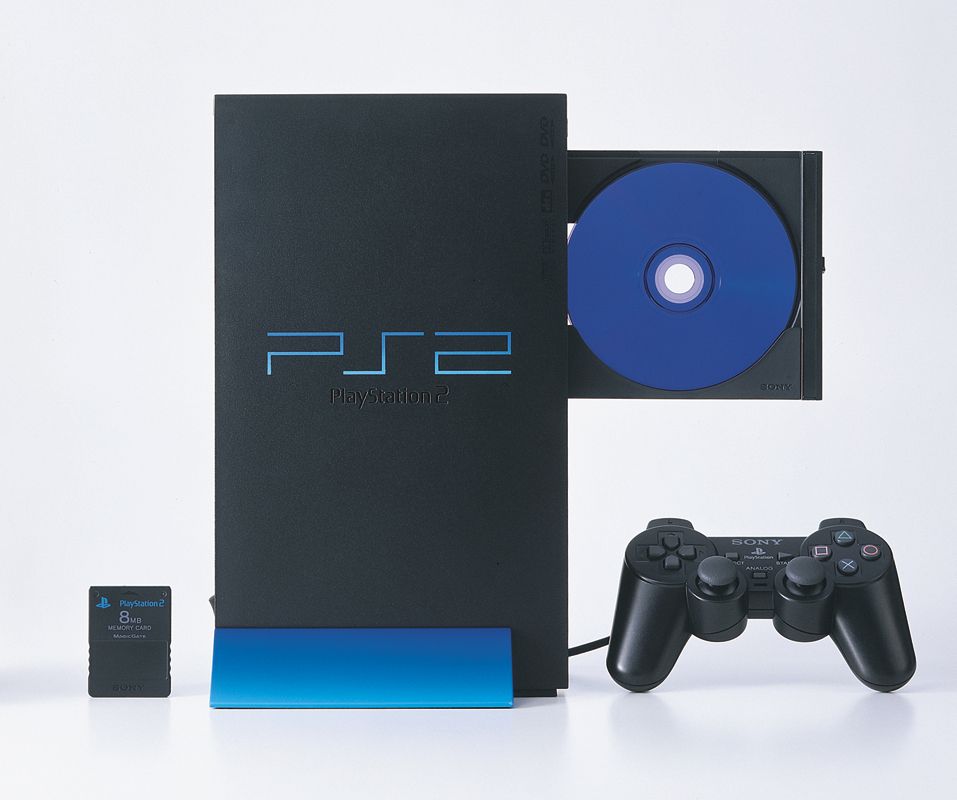 A press photograph supplied by Sony in 2000, showing the PlayStation 2 standing vertically, with the blue vertical stand attached. A blue disc is in the console's open disc tray. A control pad and memory card are also shown.
