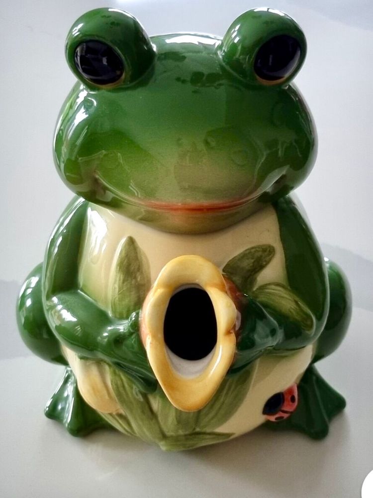 A green frog shaped novelty teapot photographed face on such that it’s spout looks like a vagina and the effect is reminiscent of a Sheela na gig 