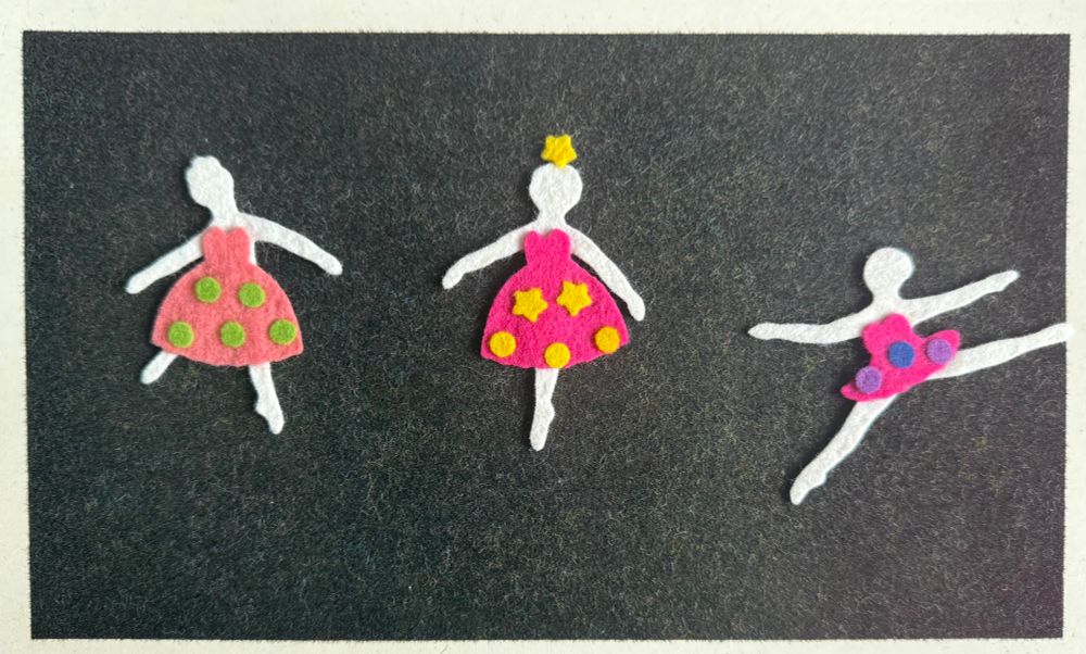 A black fuzzy felt board with three ballerina figures in pink tutus and dancing poses the middle with a star stuck to her head 