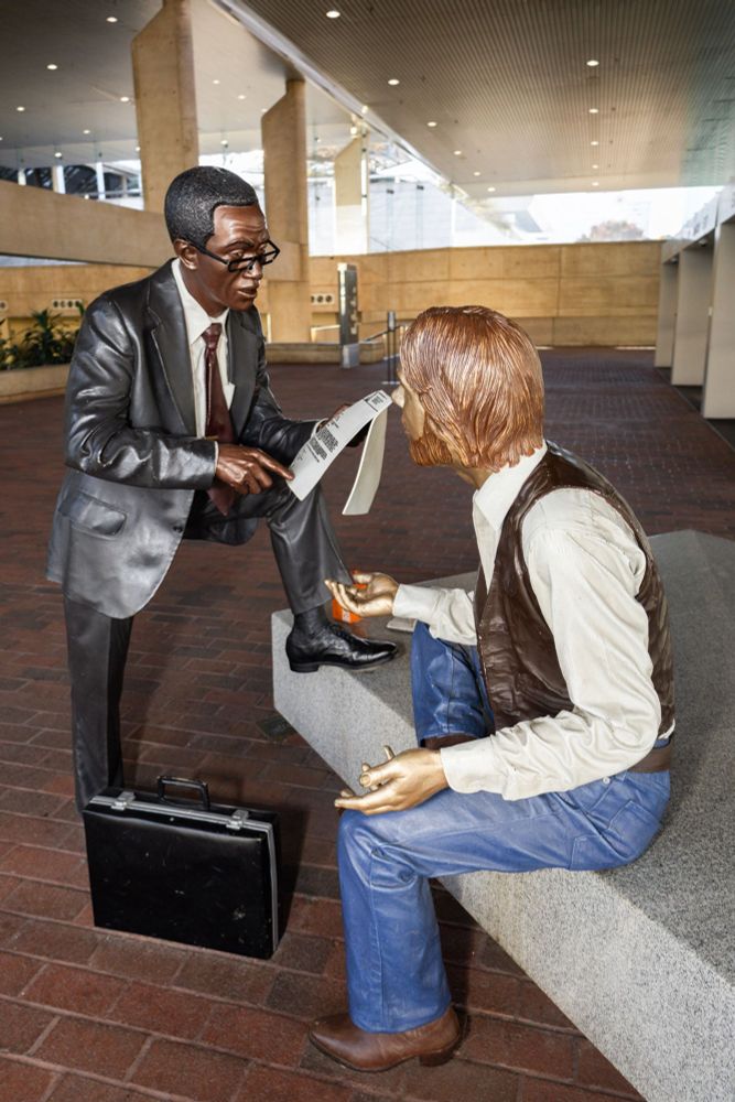 The meeting: a statue of two men having a job interview or other business meeting, surrounded by briefcases and lunch, but in a very odd 70s kind of vibe. Photographed at Baltimore Convention Center. 